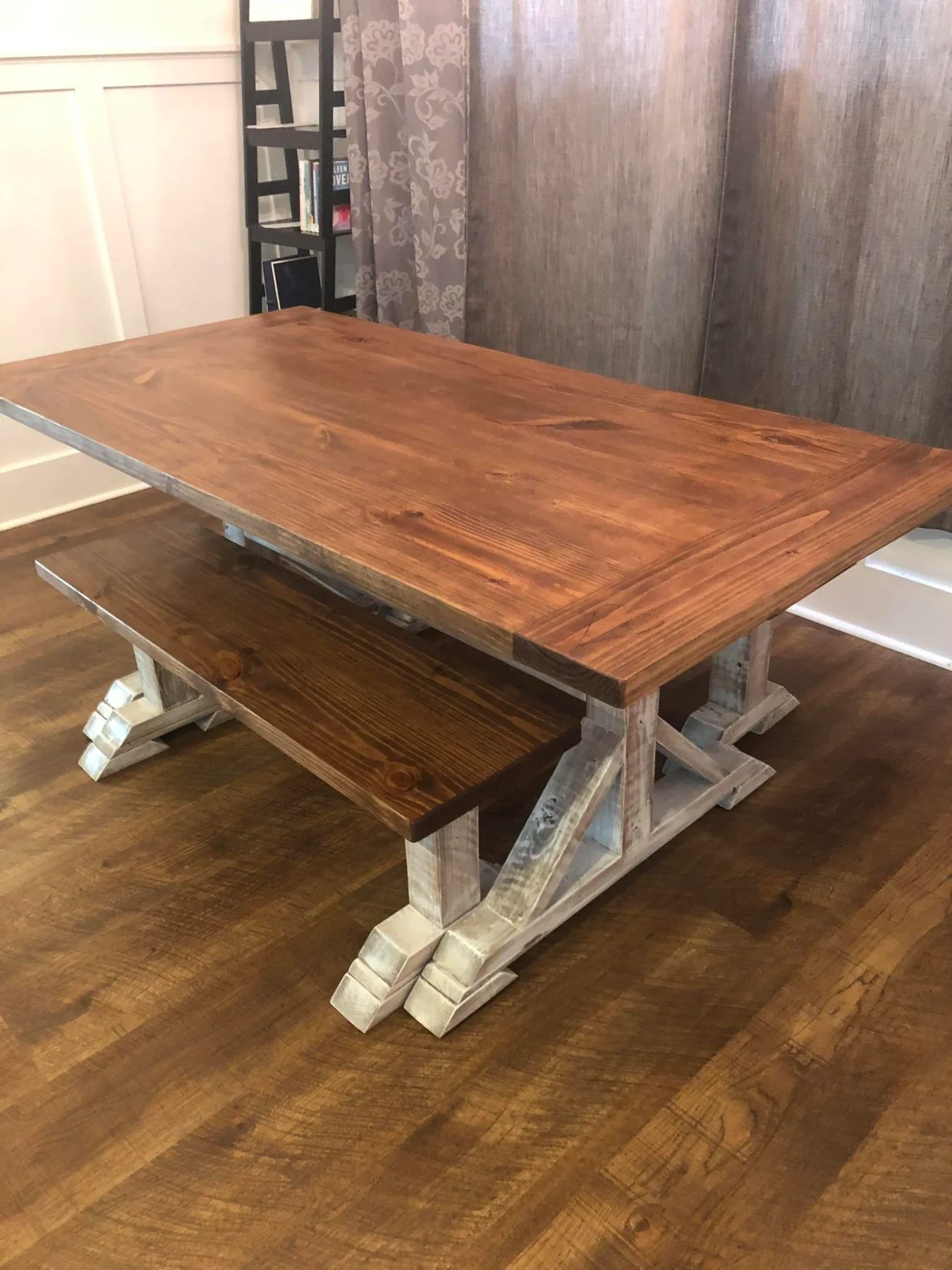 Pedestal trestle farmhouse table with a warm stained top, whitewashed trestle base, and matching bench